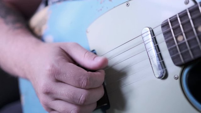 A man playing finger style on blue t-style guitar.