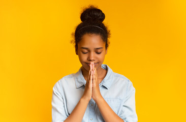 Concentrated african girl praying with hands clasped near face