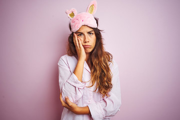 Obraz na płótnie Canvas Young woman wearing pajama and sleep mask standing over pink isolated background thinking looking tired and bored with depression problems with crossed arms.