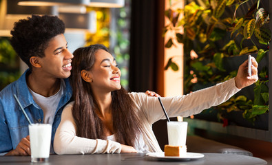 Happy mixed race teen couple making selfie at cafe