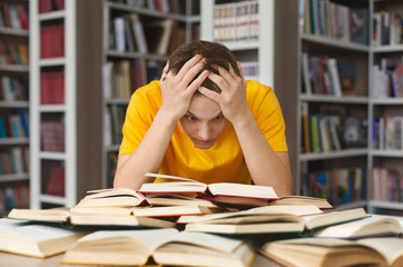 Exhausted guy holding his head and reading book in library