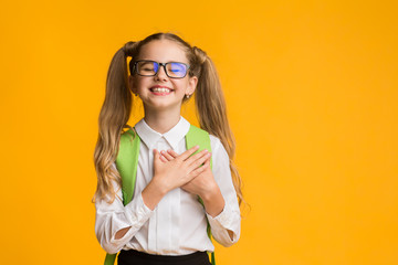 Fototapeta Cute schoolgirl posing putting hands on heart on yellow background obraz