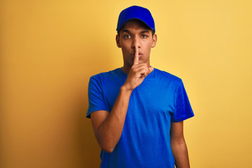 Young handsome arab delivery man standing over isolated yellow background asking to be quiet with finger on lips. Silence and secret concept.