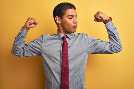 Young handsome arab businessman wearing shirt and tie over isolated yellow background showing arms muscles smiling proud. Fitness concept.