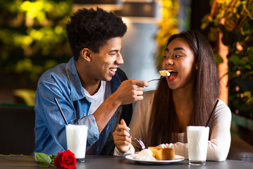 Young afro hipster feeding his girl cheesecake