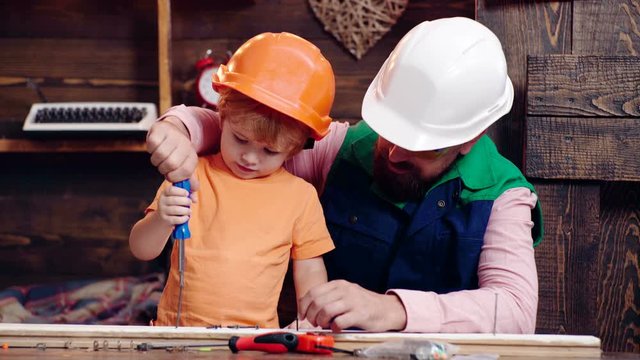 Concentrated boy exploring new stuff. Fatherhood. Father, parent teaching son to use screwdriver. Teamwork concept. Parent with busy son. Dad&son in workshop. Toddler in protective helmet in workshop.