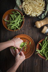 A woman is cooking vegetarian penne pasta with green beans.