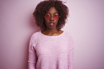 Young african afro woman wearing sweater and sunglasses over isolated pink background afraid and shocked with surprise expression, fear and excited face.