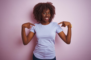 Young african afro woman wearing t-shirt standing over isolated pink background looking confident...