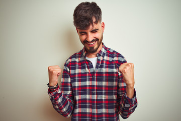 Fototapeta premium Young man wearing casual shirt standing over isolated white background very happy and excited doing winner gesture with arms raised, smiling and screaming for success. Celebration concept.