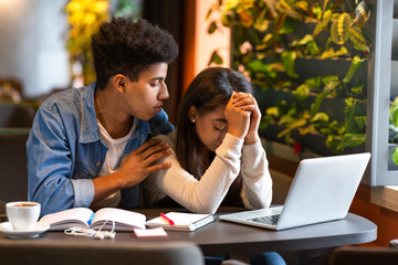 Afro guy comforting his sad girlfriend, studying together at cafeteria