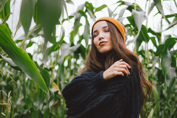 Beautiful carefree long hair asian girl witj closing eyes in the yellow hat and knitted sweater in...