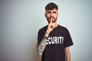 Young safeguard man with tattoo wering security uniform over isolated white background asking to be quiet with finger on lips. Silence and secret concept.