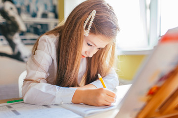 Education at home concept - Cute little girl with long hair studying or completing home work on a...