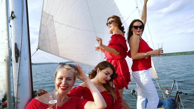 Women in red summer outfits having party with wine on sailing boat