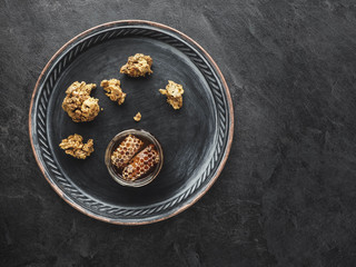 Metal plate with jar of honey and pieces of propolis on gray table. Overhead view.