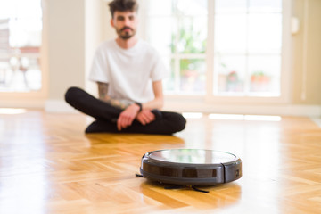 Young man using automatic vacuum cleaner to clean the floor, controling machine housework robot