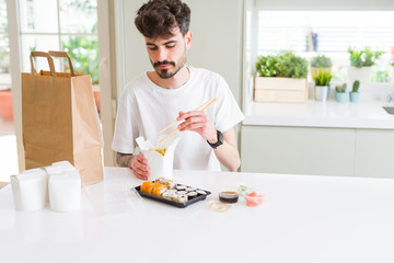 Fototapeta na wymiar Young man eating sushi asian food and noodles using choopsticks from take away delivery
