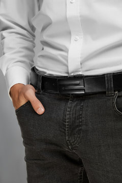 Cropped close-up shot of a man dressed in a white buttoned shirt and gray jeans with a belt. The black belt is made of textured leather and equipped with a black flat buckle 