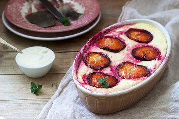 Tender curd casserole with plums and semolina, served with cinnamon and mint leaves on a wooden...