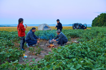 Family traveling and camping, twilight, cooking on the fire. Beautiful nature - field, forest and moon.