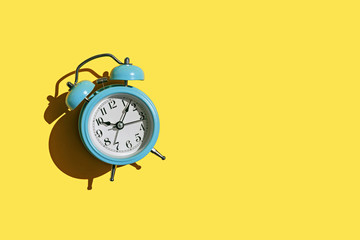 Blue alarm clock on yellow background with copy space.