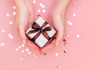 Woman's hands with manicure hold gift box with brown ribbon on pale pink background. Festive...