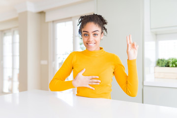 Beautiful african american woman with afro hair wearing a casual yellow sweater smiling swearing...
