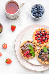 Sweet tartlets with berries and tea on light table
