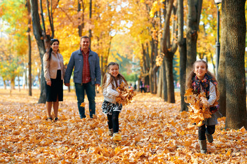 Happy family having holiday in autumn city park. Children and parents posing, smiling, playing and having fun. Bright yellow trees and leaves