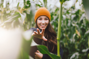 Beautiful carefree long hair asian girl in the yellow hat and knitted sweater in autumn corn field. Selective focus on hand. Sensitivity to nature concept