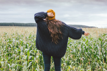 Beautiful carefree long hair asian girl in the yellow hat and knitted sweater from behind in autumn...