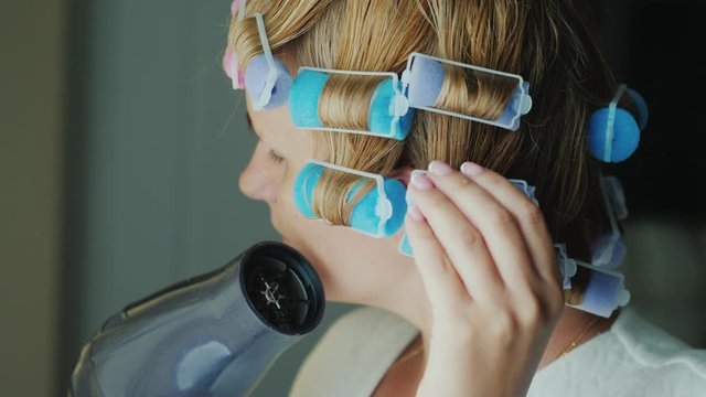 Woman with curlers on her head dries hair with a hairdryer
