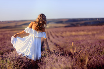 Fototapeta na wymiar Beautiful girl on the lavender field. Beautiful woman in the lavender field on sunset.