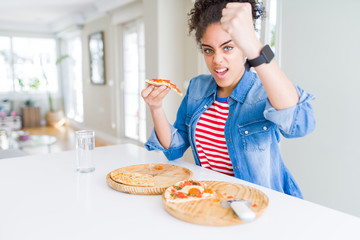 Young african american woman eating two homemade cheese pizzas annoyed and frustrated shouting with anger, crazy and yelling with raised hand, anger concept