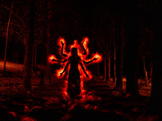 Image of woman in the dark forest silhouetted with red fire effect on the sides