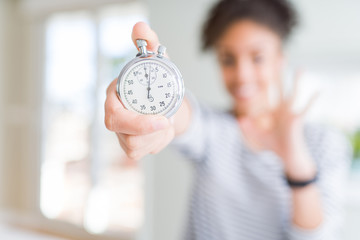 Young african american woman holding stopwatch doing ok sign with fingers, excellent symbol