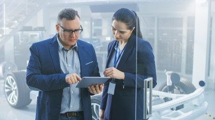 Female and Male Engineer Work in a High Tech Development Facility Holding a Tablet Computer. They...