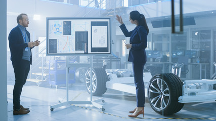 Male and Female Design Engineers are Working and Discuss Electric Car Benefits on an Interactive...