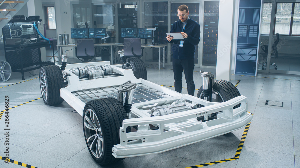 Aufkleber Engineer with Glasses and Beard Scans Electric Car Chassis Prototype with Wheels, Batteries and Engine with an Augmented Reality Software on a Tablet Computer in a High Tech Development Laboratory.