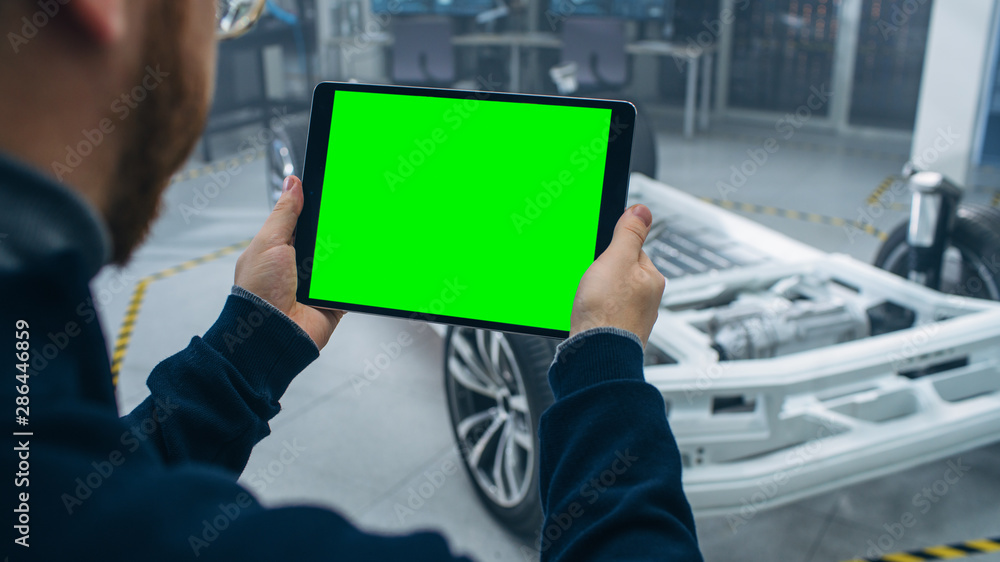 Aufkleber Engineer with Glasses and Beard Scans Electric Car Chassis Prototype with Wheels, Batteries and Engine with an Augmented Reality Software on a Tablet Computer in a High Tech Development Laboratory.