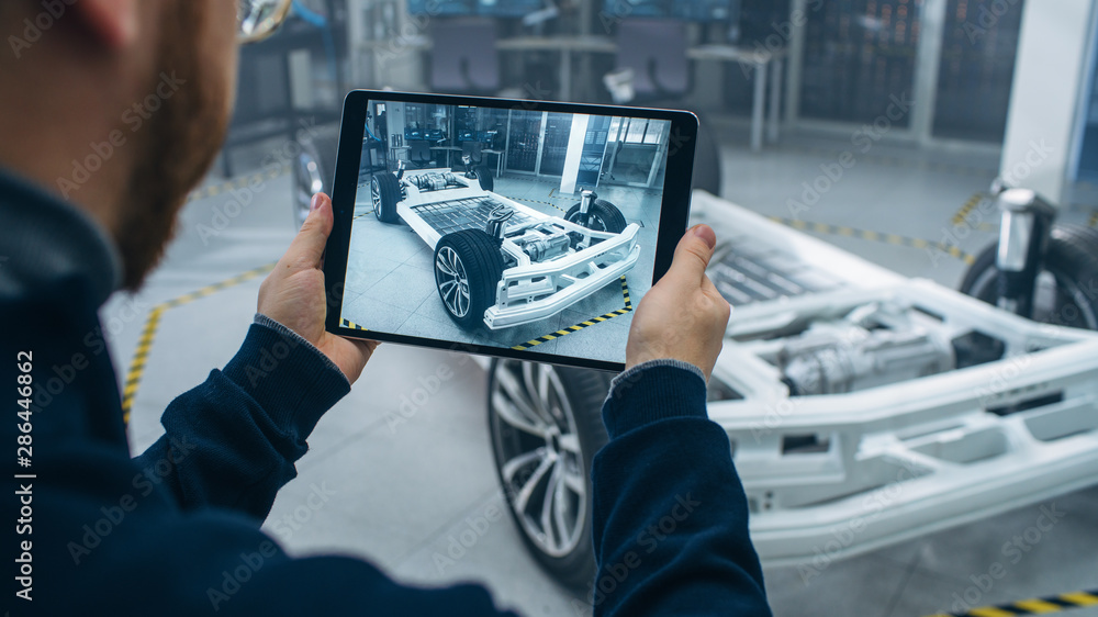 Leinwandbilder Engineer with Glasses and Beard Scans Electric Car Chassis Prototype with Wheels, Batteries and Engine with an Augmented Reality Software on a Tablet Computer in a High Tech Development Laboratory.