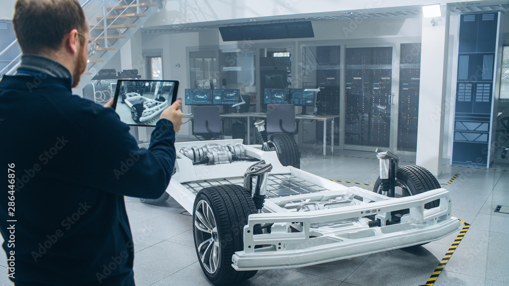 Aufkleber Engineer with Glasses and Beard Scans Electric Car Chassis Prototype with Wheels, Batteries and Engine with an Augmented Reality Software on a Tablet Computer in a High Tech Development Laboratory.