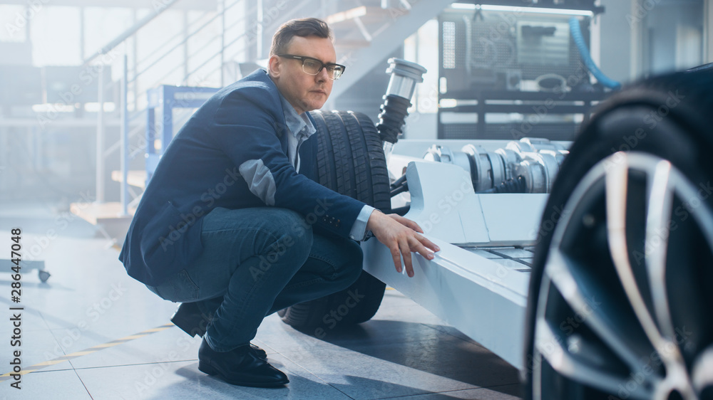 Leinwandbilder engineer with glasses works with an electric car chassis prototype with wheels, batteries and engine