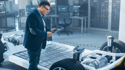 Automotive Design Engineer Looking at Technical Drawing of an Electric Car Chassis Prototype on a...