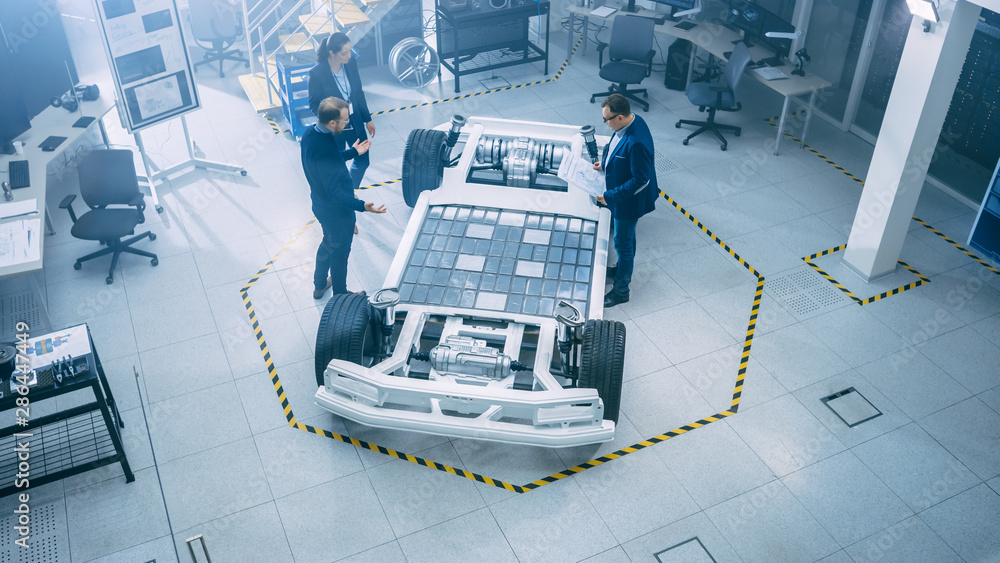 Poster automotive design engineers talking while working on electric car chassis prototype. in innovation l