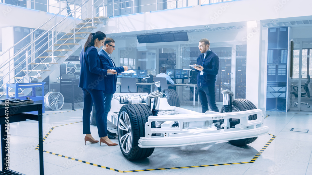 Poster automotive design engineers looking at technical drawings of a electric car chassis prototype. in in