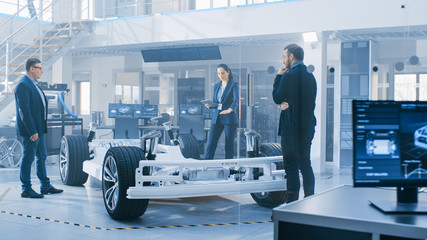 Automotive Design Engineers Talking while Working on Electric Car Chassis Prototype. In Innovation...