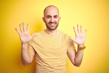 Naklejka premium Young bald man with beard wearing casual striped t-shirt over yellow isolated background showing and pointing up with fingers number ten while smiling confident and happy.