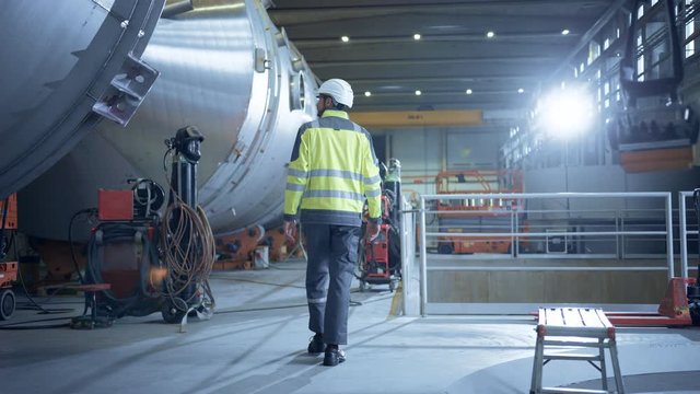 Following Shot of Heavy Industry Engineer Walking through Pipe Manufacturing Factory. Modern Facility for Design and Construction of Large Diameter Oil, Gas and Fuels Transport Pipeline. Slow Motion